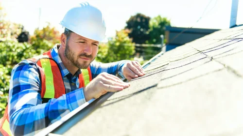 Roofer inspecting shingles on a residential roof in Fayetteville, Arkansas