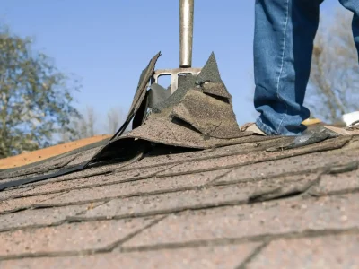 Roofer inspecting storm-damaged asphalt shingles on a roof in Arkansas