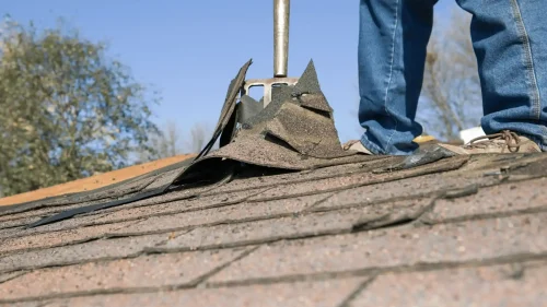 Roofer inspecting storm-damaged asphalt shingles on a roof in Arkansas