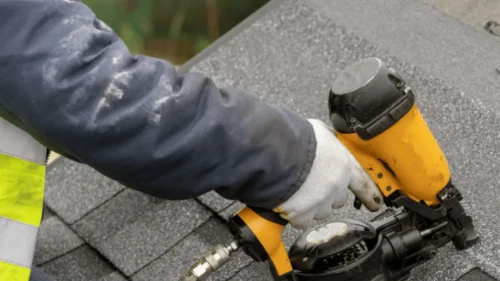 Roofer using nail gun to install new asphalt shingles during full roof replacement in Northwest Arkansas